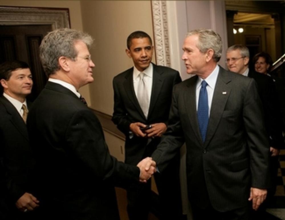 Bush kättelee ja Obama on taustalla.